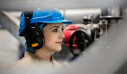 A woman in a blue helmet and earphones framed through the metal bars of a machine