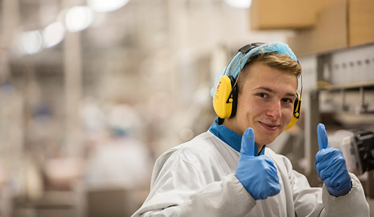 A man with earphones and blue gloves gives a thumbs up in a laboratory